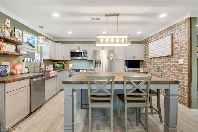 kitchen featuring sink, wooden counters, decorative light fixtures, a center island, and stainless steel appliances