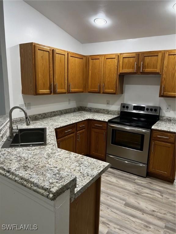 kitchen featuring electric stove, sink, light stone countertops, kitchen peninsula, and light wood-type flooring