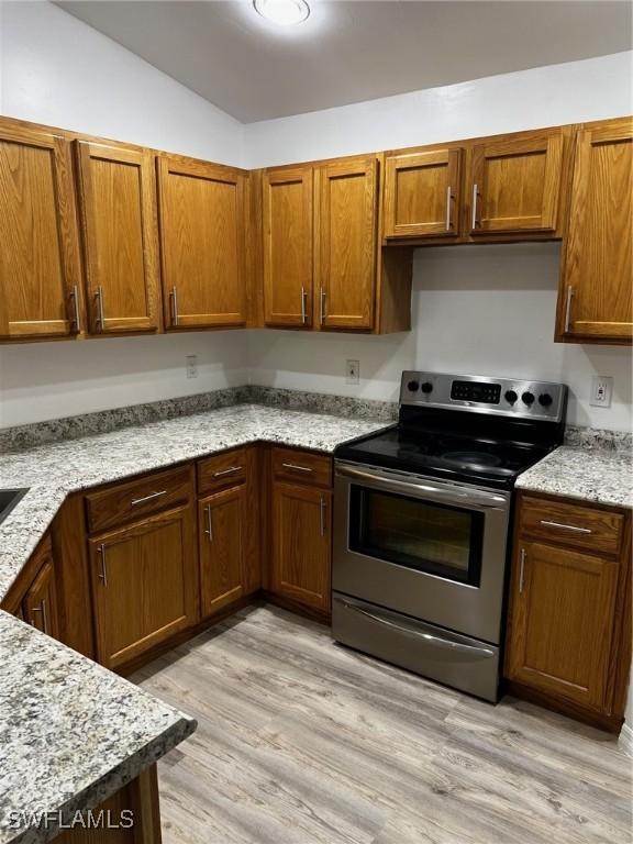 kitchen with light stone counters, stainless steel range with electric cooktop, and light hardwood / wood-style floors