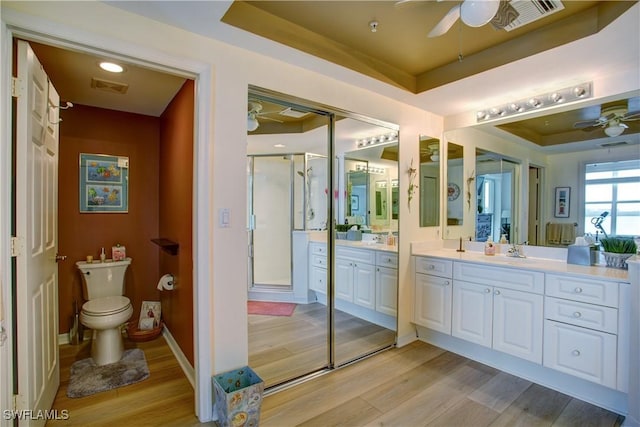 bathroom with hardwood / wood-style flooring, ceiling fan, vanity, a raised ceiling, and toilet