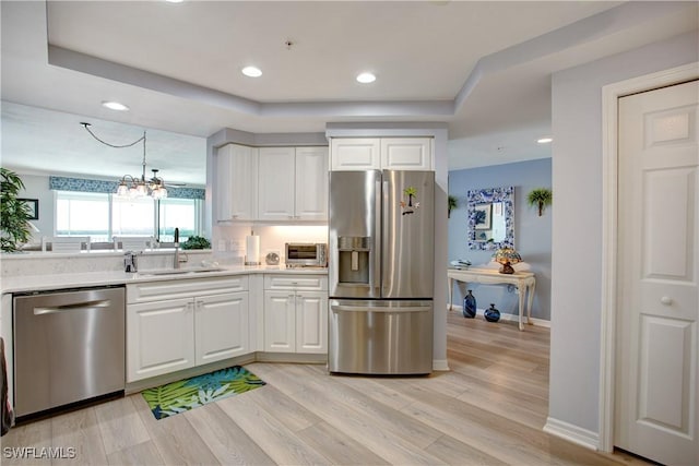 kitchen featuring sink, light hardwood / wood-style flooring, appliances with stainless steel finishes, white cabinetry, and decorative light fixtures