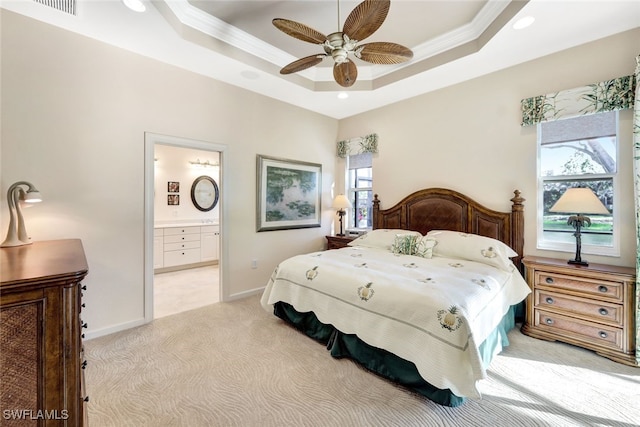 carpeted bedroom with a tray ceiling, ornamental molding, ceiling fan, and ensuite bathroom