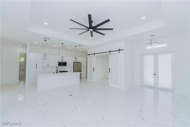 unfurnished living room with sink, ceiling fan, a raised ceiling, a barn door, and french doors