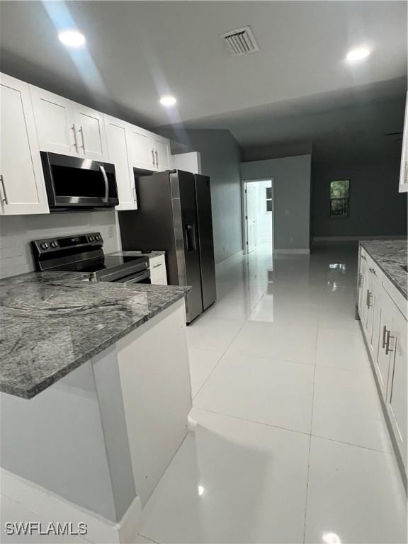 kitchen featuring stainless steel appliances, white cabinetry, light tile patterned floors, and dark stone counters