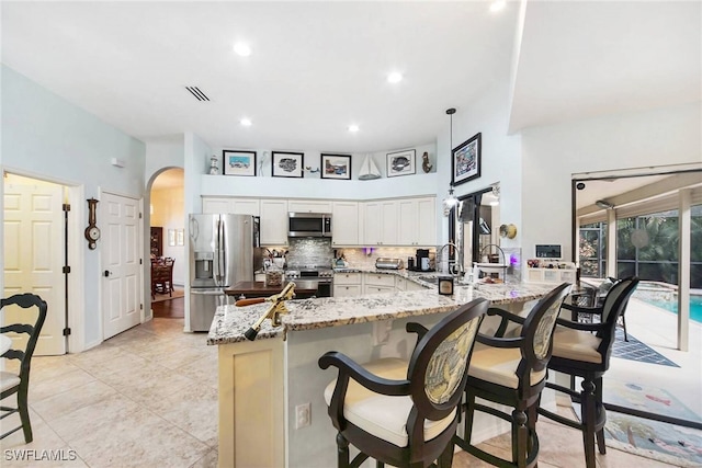 kitchen with backsplash, white cabinets, light stone counters, kitchen peninsula, and stainless steel appliances