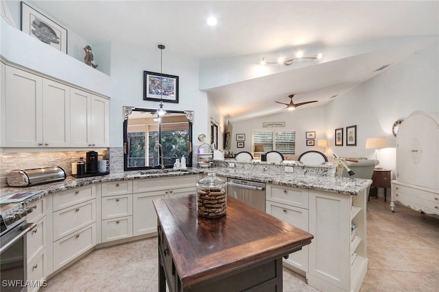 kitchen featuring pendant lighting, ceiling fan, appliances with stainless steel finishes, a center island, and light stone counters