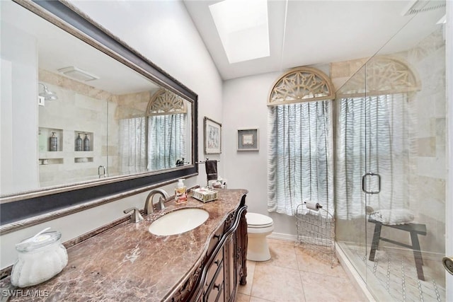 bathroom with a shower with door, a skylight, vanity, tile patterned floors, and toilet