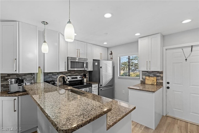 kitchen with white cabinetry, decorative light fixtures, dark stone countertops, appliances with stainless steel finishes, and kitchen peninsula