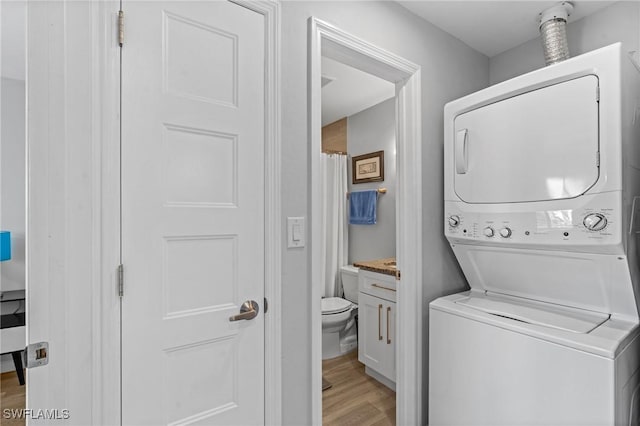 clothes washing area with stacked washer and clothes dryer and light wood-type flooring