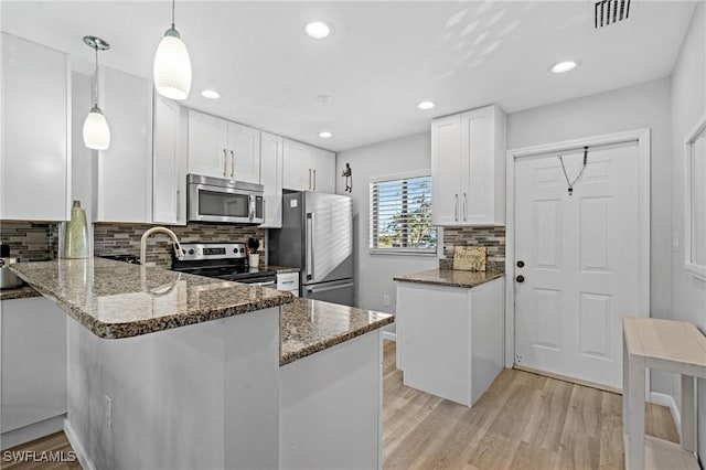 kitchen with white cabinetry, appliances with stainless steel finishes, hanging light fixtures, and dark stone countertops