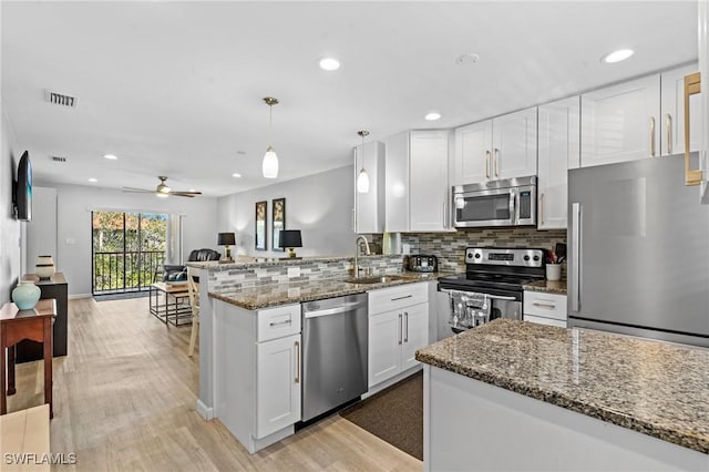 kitchen with stone countertops, decorative light fixtures, kitchen peninsula, stainless steel appliances, and white cabinets