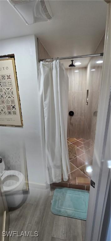 bathroom with hardwood / wood-style floors, toilet, and a shower with shower curtain