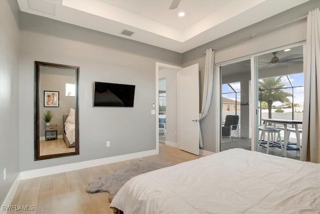 bedroom with ceiling fan, a tray ceiling, light hardwood / wood-style flooring, and access to outside