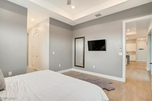 bedroom featuring ceiling fan, a raised ceiling, and light hardwood / wood-style flooring