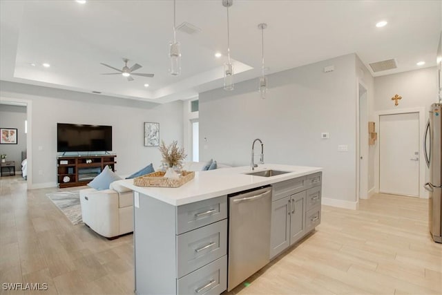 kitchen featuring pendant lighting, a raised ceiling, sink, a kitchen island with sink, and stainless steel appliances