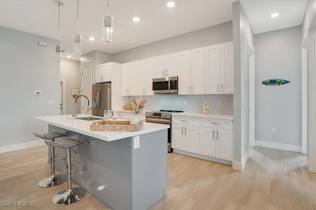 kitchen featuring sink, stainless steel appliances, an island with sink, white cabinets, and decorative light fixtures