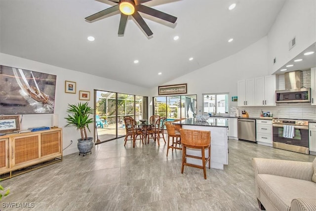 kitchen with wall chimney exhaust hood, a breakfast bar area, white cabinetry, tasteful backsplash, and appliances with stainless steel finishes