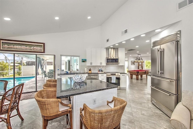 kitchen featuring appliances with stainless steel finishes, white cabinetry, high vaulted ceiling, tasteful backsplash, and dark stone counters