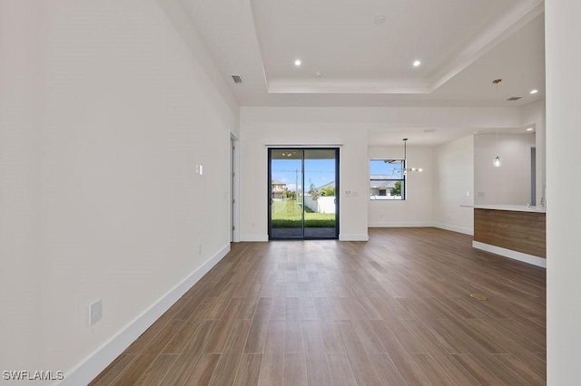 unfurnished living room featuring a raised ceiling, hardwood / wood-style floors, and a notable chandelier