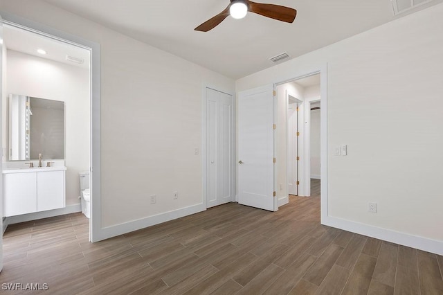 unfurnished bedroom with connected bathroom, sink, hardwood / wood-style floors, and ceiling fan