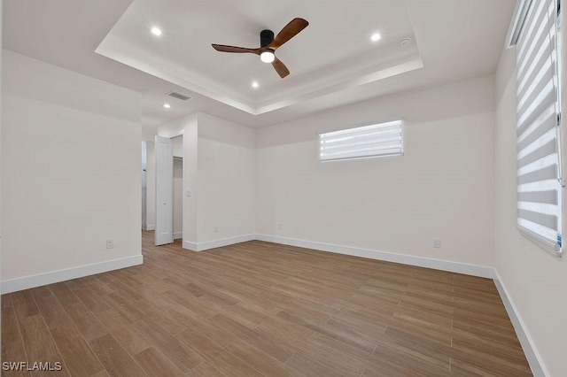 empty room with ceiling fan, a raised ceiling, and hardwood / wood-style floors