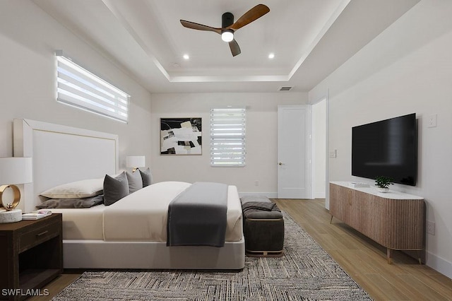 bedroom with ceiling fan, a raised ceiling, hardwood / wood-style floors, and multiple windows