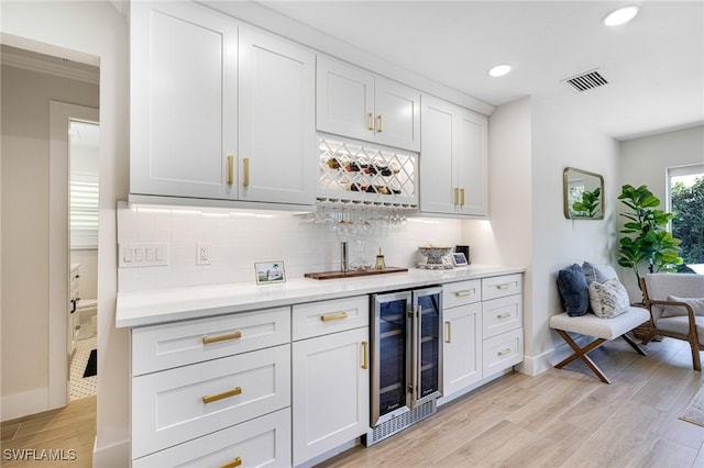 bar with tasteful backsplash, white cabinets, beverage cooler, and light wood-type flooring