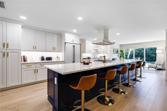 kitchen with high end fridge, island range hood, an island with sink, and white cabinets