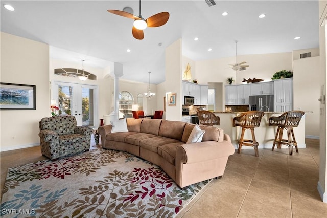 living room with french doors, decorative columns, high vaulted ceiling, light tile patterned floors, and ceiling fan with notable chandelier