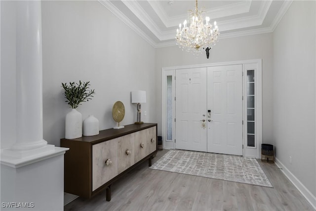 entryway featuring ornate columns, crown molding, light wood-type flooring, a raised ceiling, and a notable chandelier