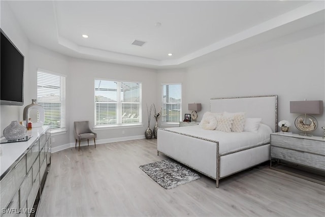 bedroom featuring multiple windows, a raised ceiling, and light wood-type flooring