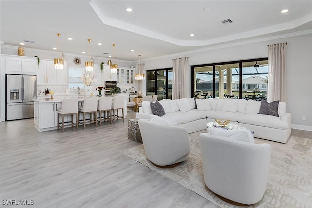 living room with ornamental molding, a tray ceiling, sink, and light hardwood / wood-style flooring