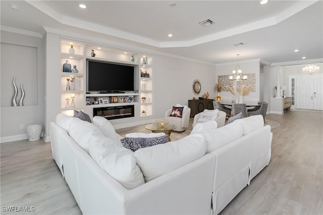 living room featuring light hardwood / wood-style flooring, ornamental molding, a tray ceiling, an inviting chandelier, and built in shelves