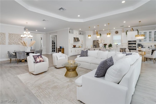 living room featuring a tray ceiling, a notable chandelier, crown molding, and light wood-type flooring