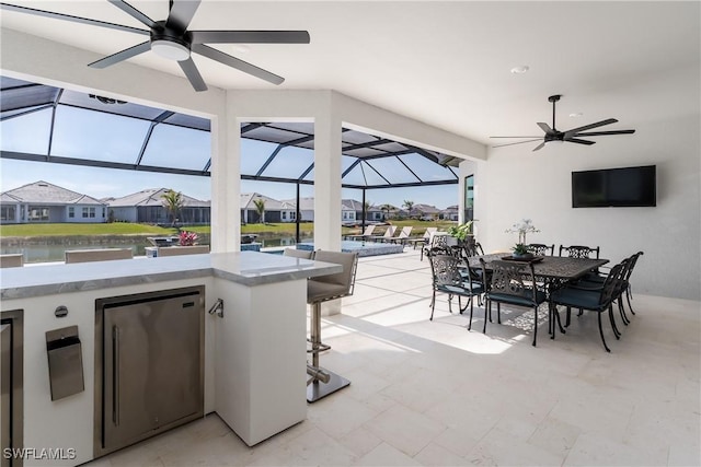 view of patio with a water view, ceiling fan, a lanai, and an outdoor bar