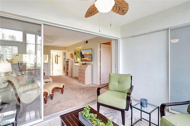 sitting room with ceiling fan, a textured wall, carpet flooring, and visible vents