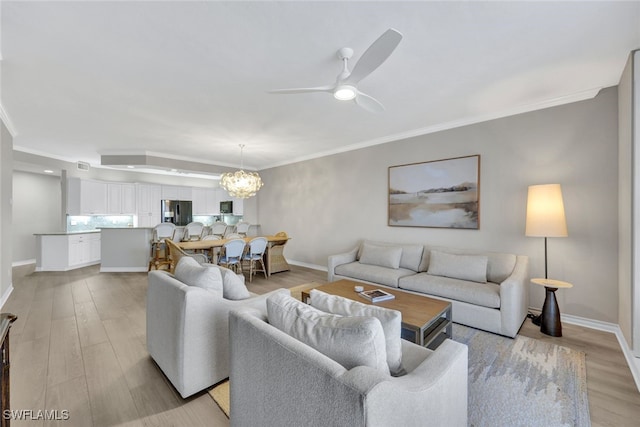 living room featuring light wood-style flooring, ornamental molding, baseboards, and ceiling fan with notable chandelier