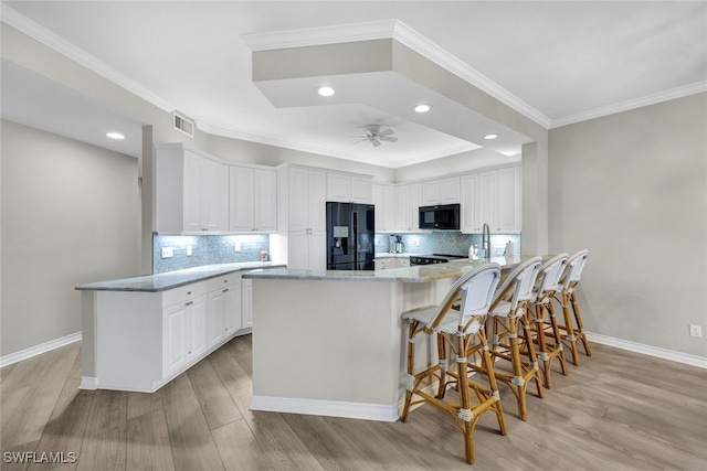 kitchen with a ceiling fan, a peninsula, black appliances, and light wood finished floors