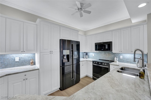 kitchen featuring black appliances, white cabinetry, light stone counters, and a sink