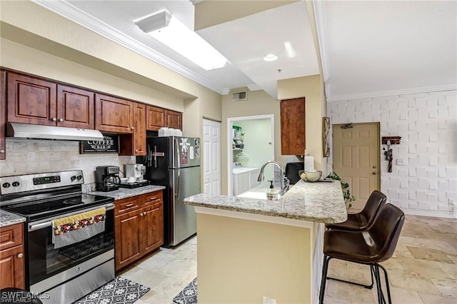 kitchen with crown molding, a kitchen breakfast bar, stainless steel appliances, light stone countertops, and washer and clothes dryer