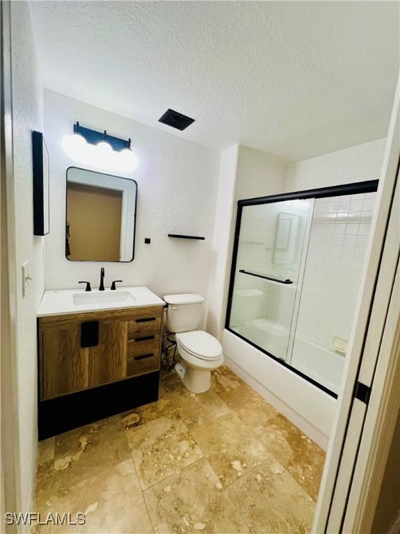 full bathroom featuring enclosed tub / shower combo, vanity, toilet, and a textured ceiling