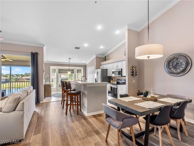 dining room featuring vaulted ceiling, ornamental molding, and light hardwood / wood-style floors