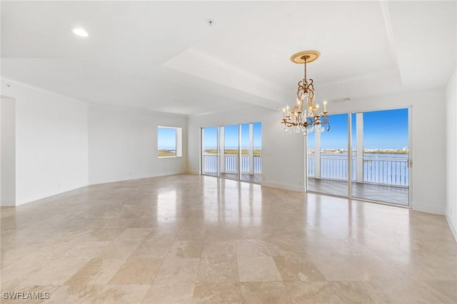 empty room with a tray ceiling, a chandelier, and a water view