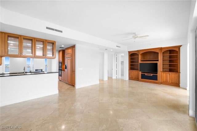 unfurnished living room featuring built in shelves, ceiling fan, and sink