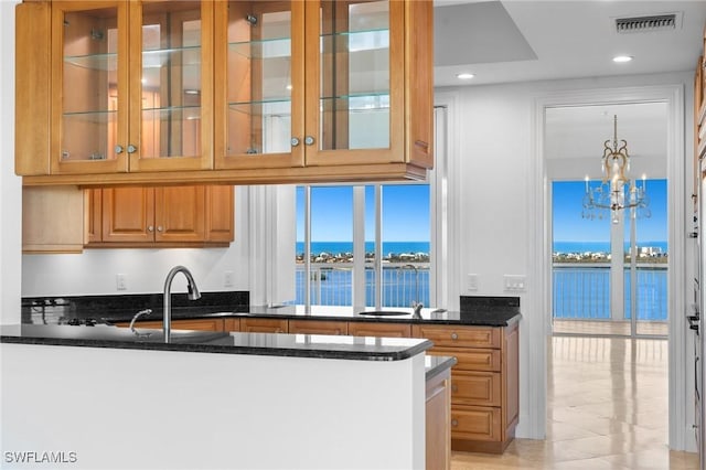 kitchen with sink, a water view, decorative light fixtures, dark stone countertops, and kitchen peninsula