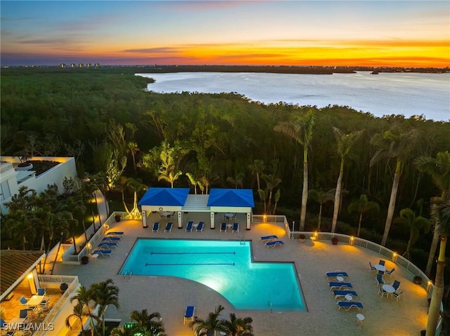 pool at dusk featuring a patio and a water view