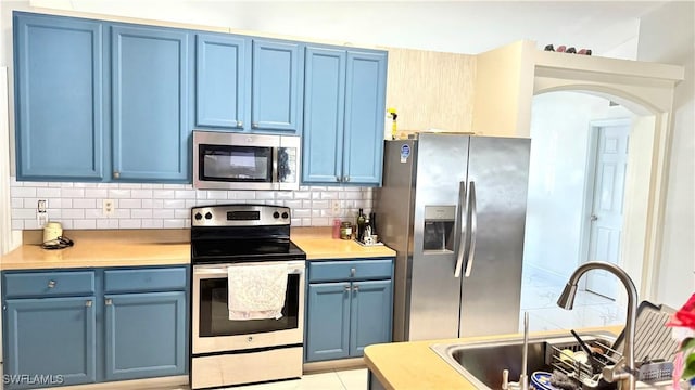 kitchen with appliances with stainless steel finishes, sink, backsplash, light tile patterned floors, and blue cabinetry