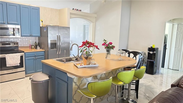 kitchen featuring sink, blue cabinetry, stainless steel appliances, tasteful backsplash, and a kitchen bar