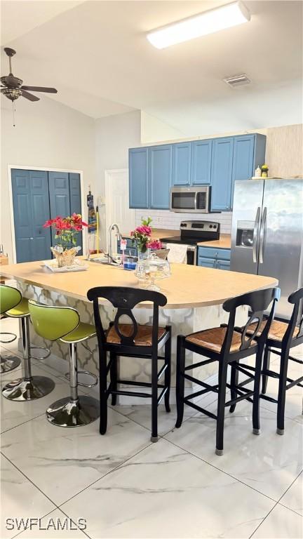 kitchen with lofted ceiling, blue cabinets, a breakfast bar, stainless steel appliances, and decorative backsplash