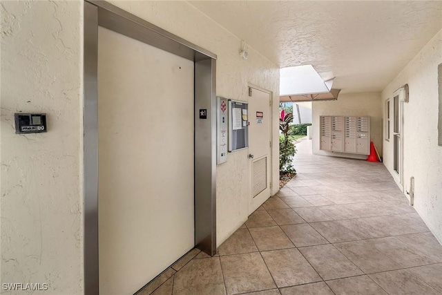 corridor featuring a textured ceiling, a mail area, elevator, and light tile patterned flooring